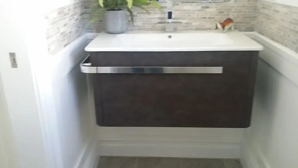 Dark floating vanity with an integrated sink and wall mounted faucet