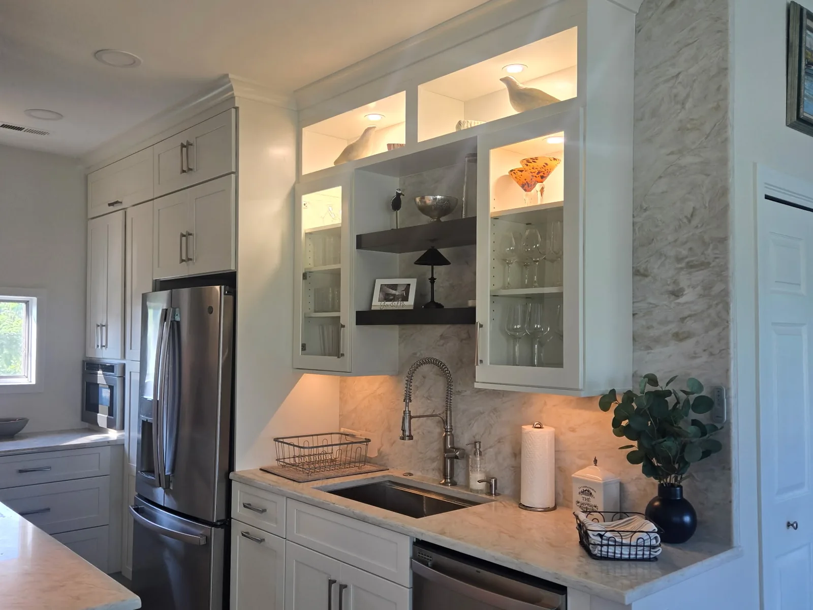 Lit glass front upper cabinets above a prep sink run in the same kitchen